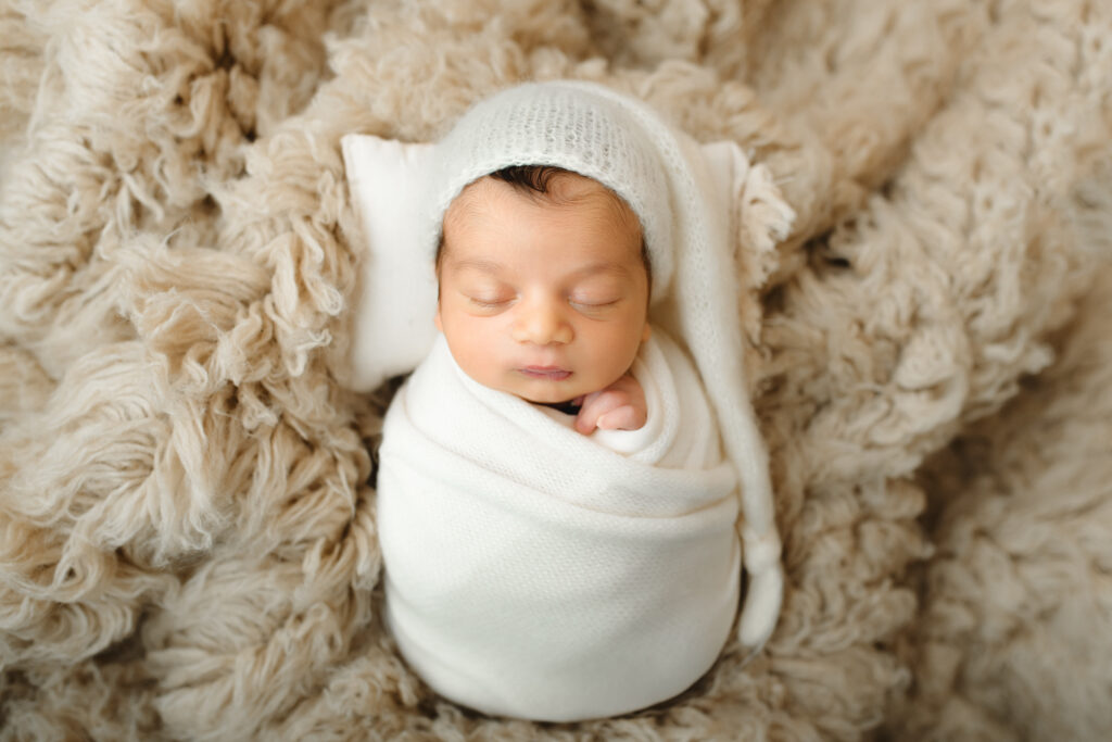 Newborn boy wrapped with a knit blanket on a wool blanket. 