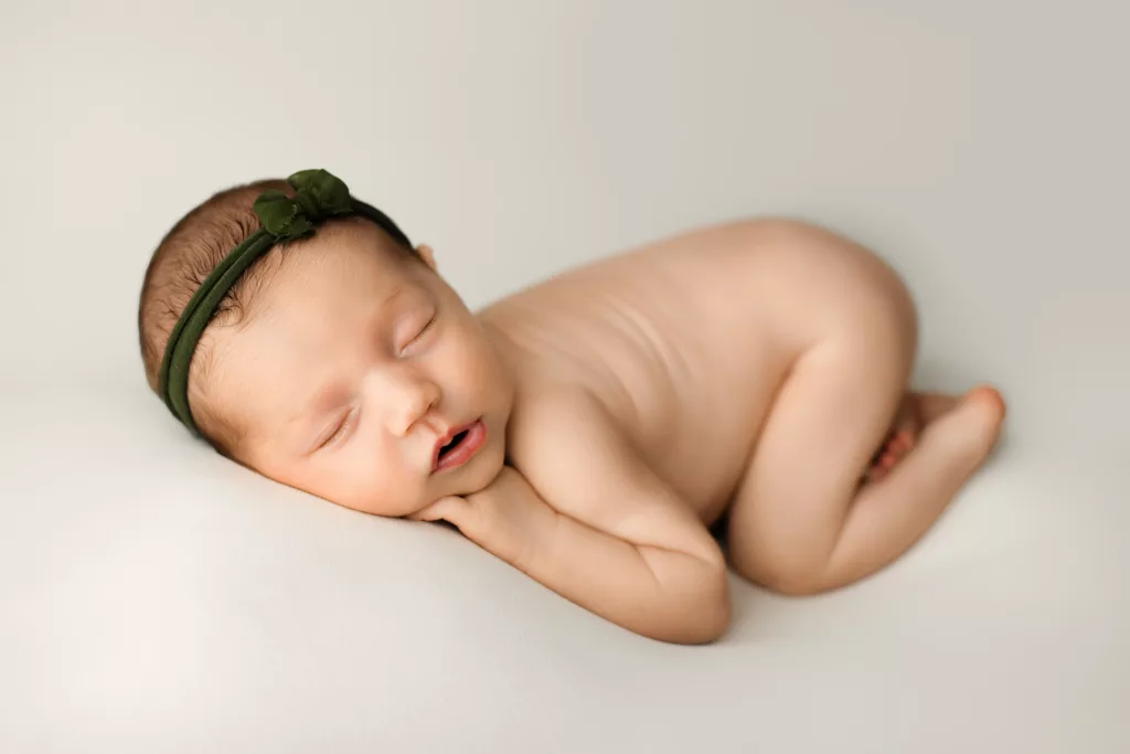 newborn baby posed on her belly with her legs tucked under her. 