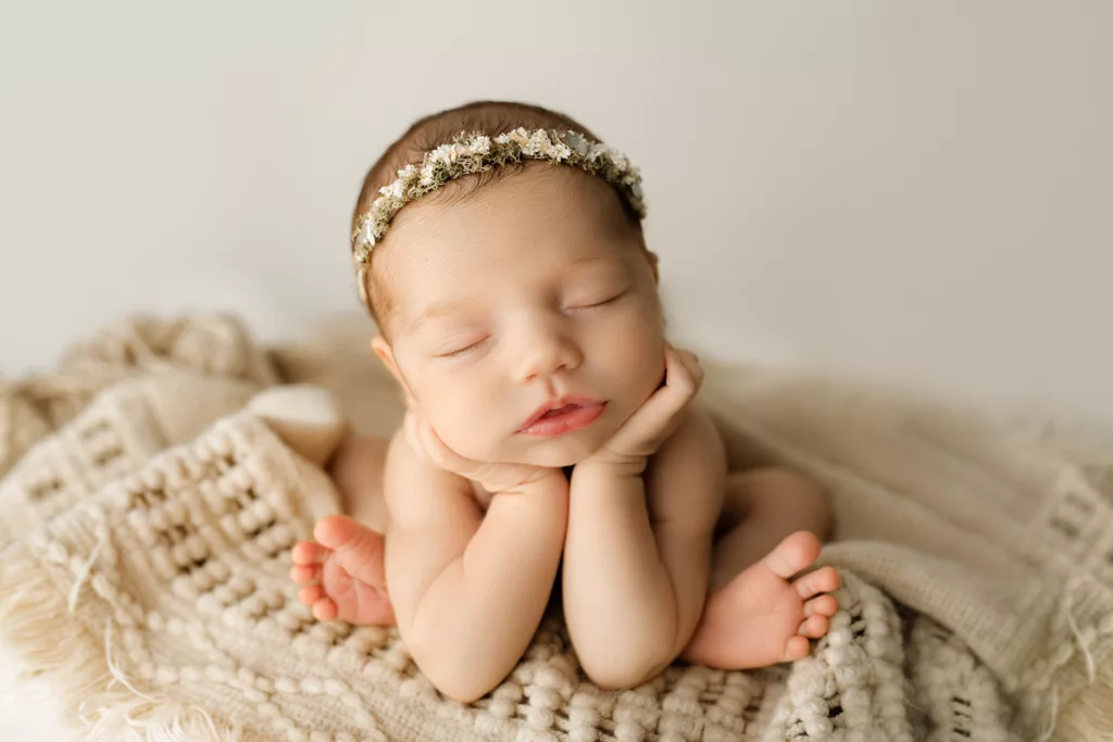 newborn baby girl posed sitting on a blanket holding her head